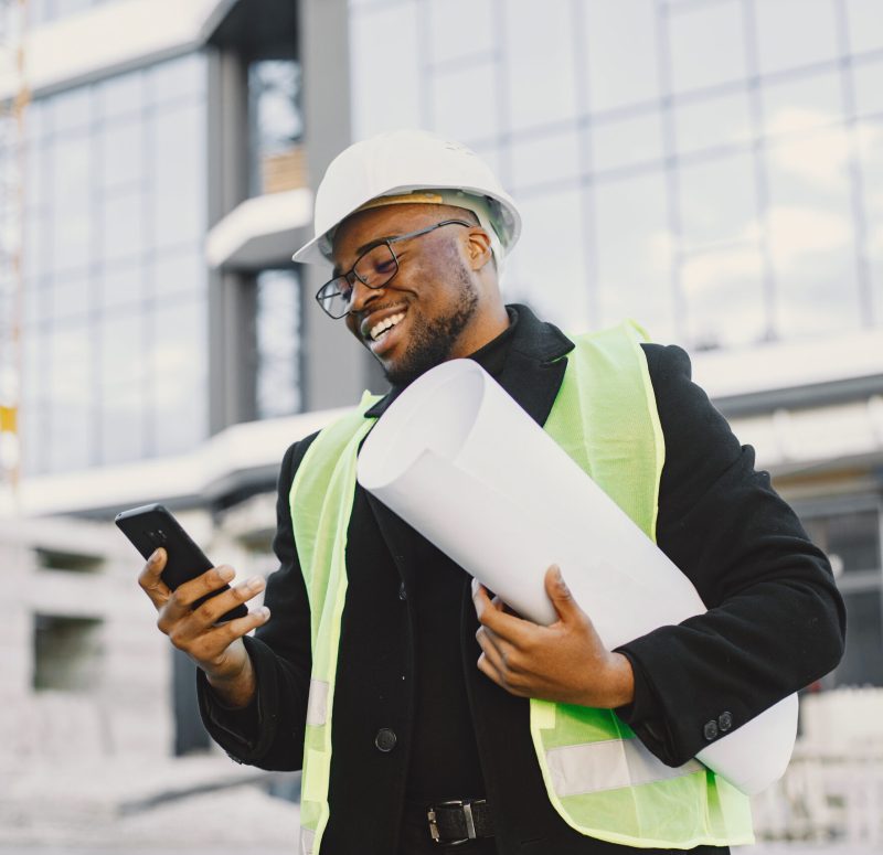 Black architect with project talk by phone Young black race man with blueprint stading near glass building. Talking by phone.